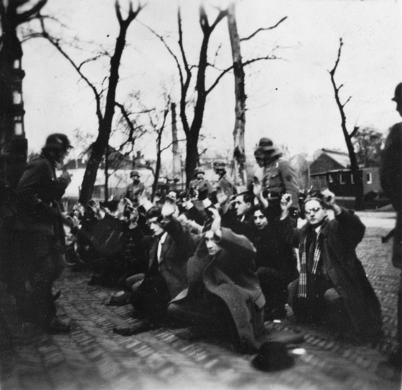 Jewish men kneeling on the cobbles with their hands raised, guarded by German soldiers, during the raid on the Jonas Daniel Meijerplein in Amsterdam in February 1941