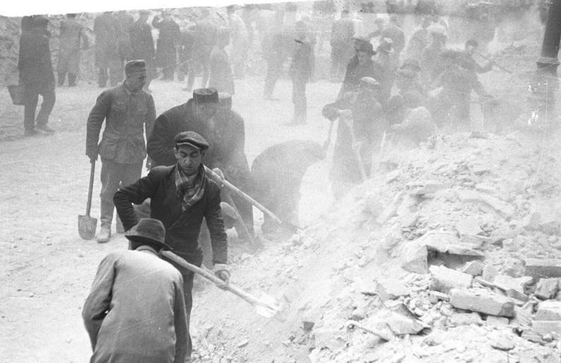Jews carrying out forced clearing work in the streets of Warsaw under German guard.