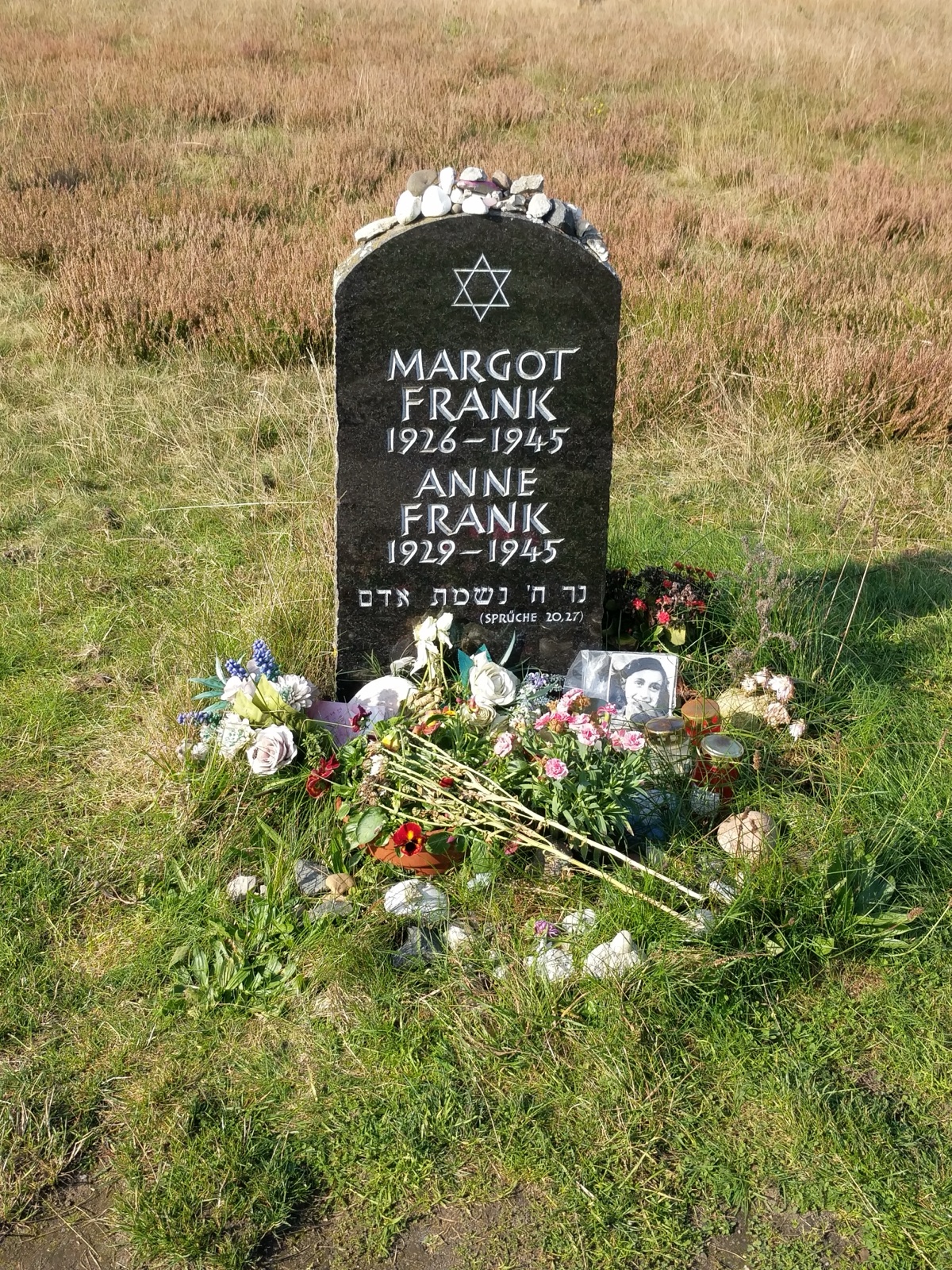 A flat pale stone slab on heather-covered ground, carved with the sisters' names and dates, small stones and flowers left on its surface.