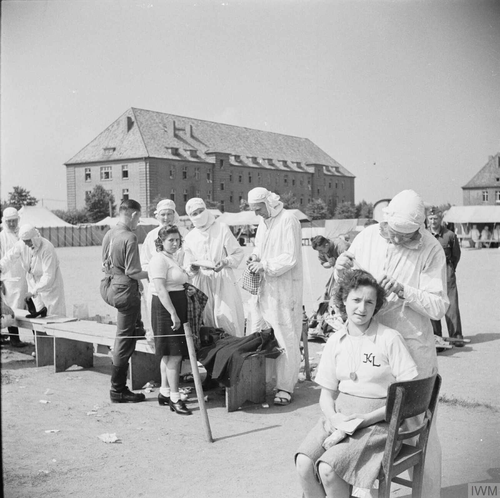 Three young women in gowns stand together in a bare hospital room while a nurse in an apron attends to one of them.