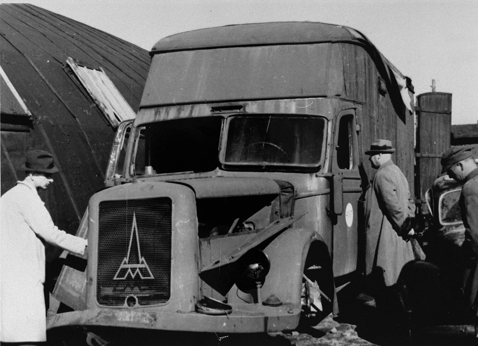 A burned-out box-bodied truck standing in a yard, its panels stripped back to the frame.