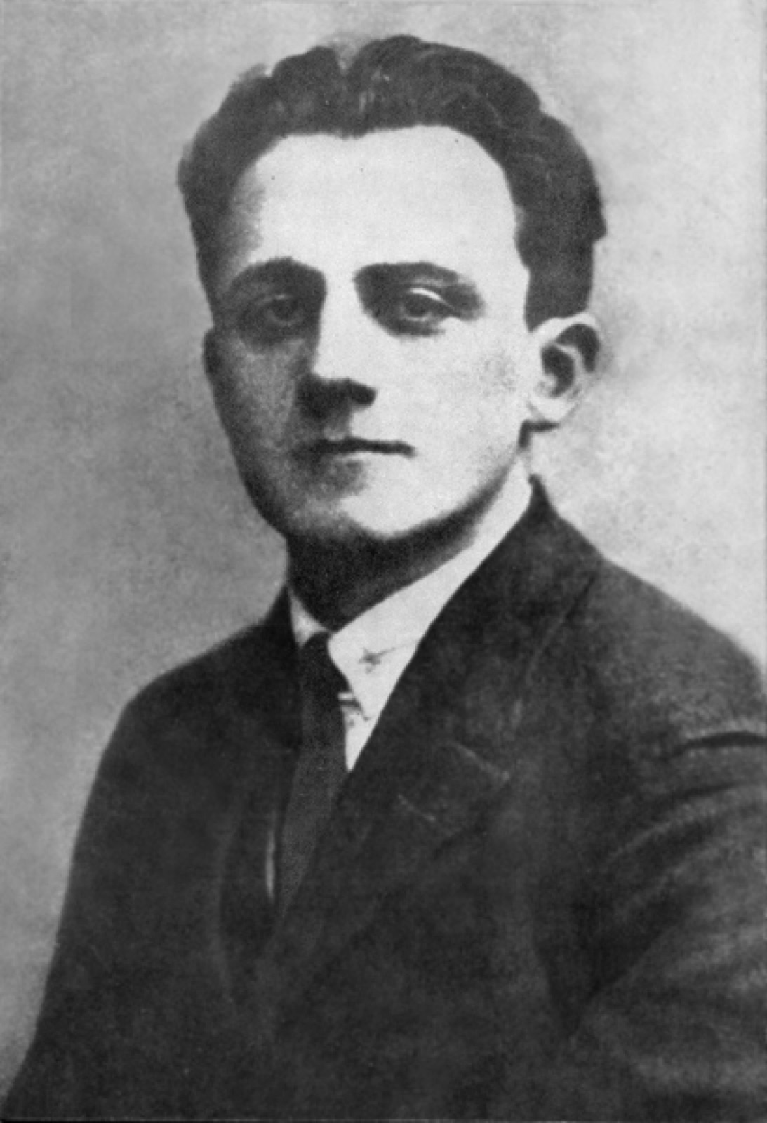 Head-and-shoulders portrait of a man in a jacket and tie, facing the camera, photographed against a plain background.