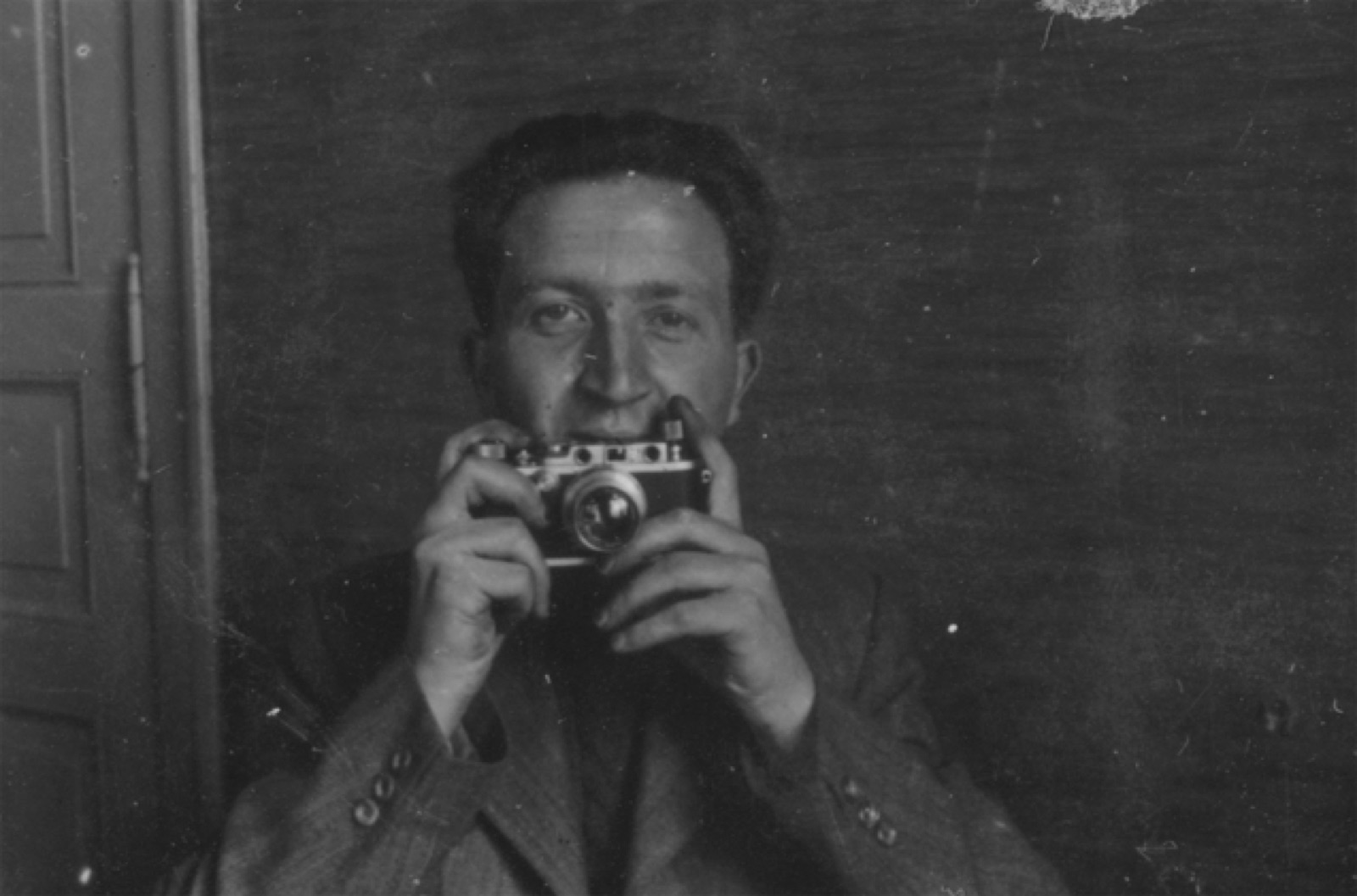 A man photographing his own reflection in a mirror, camera raised to his face.
