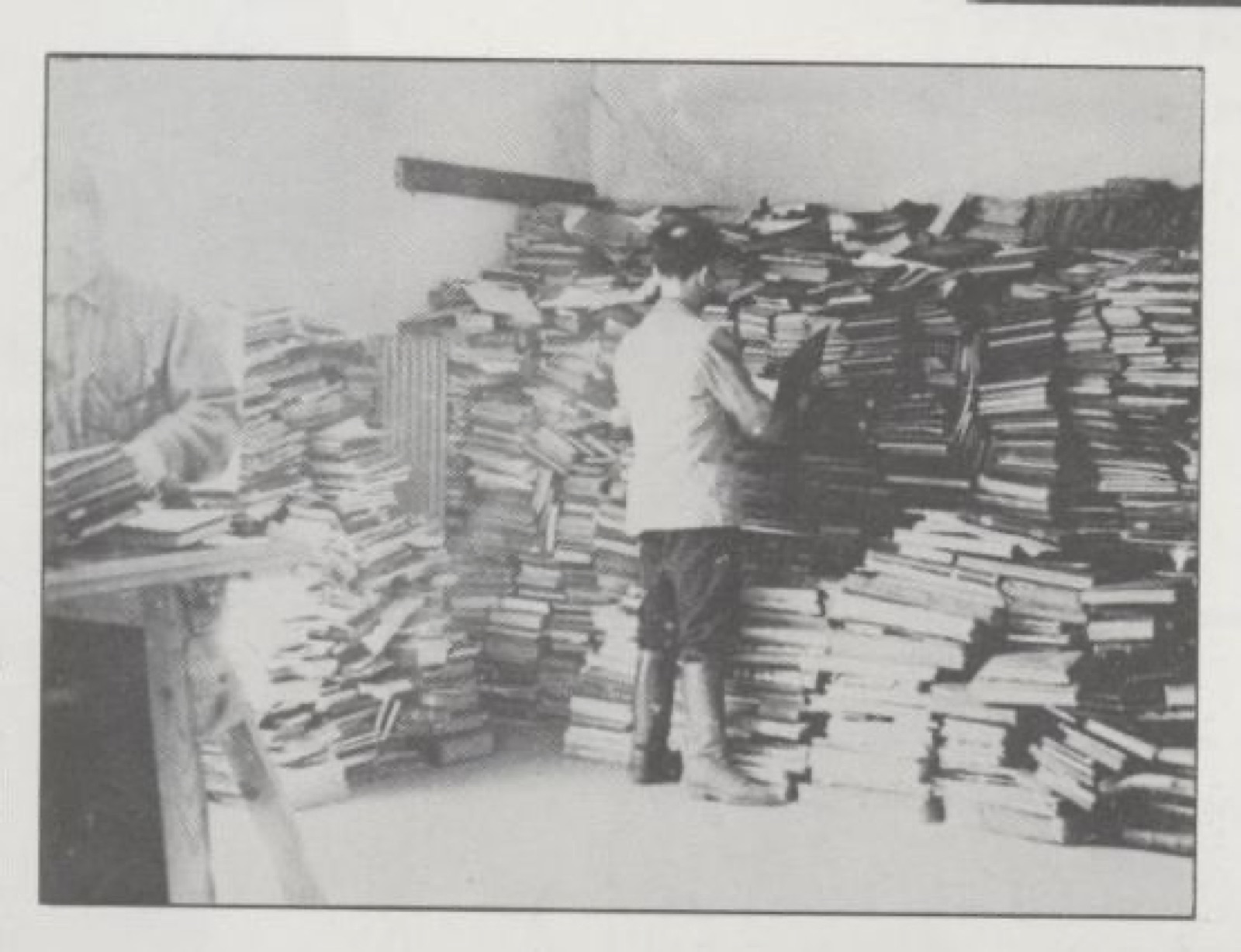 A man in a jacket standing beside shelved and stacked old books in a museum room.