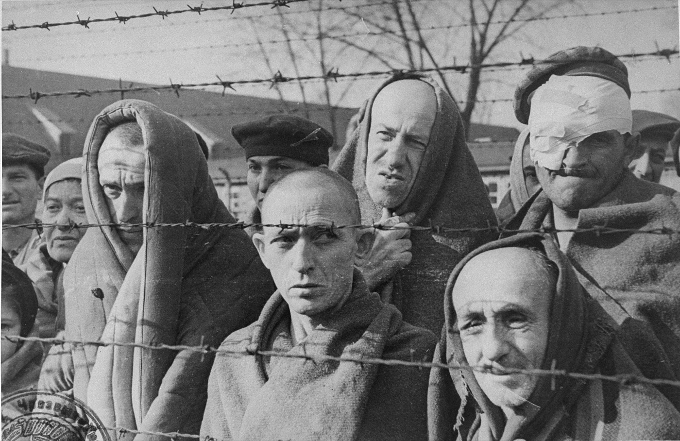 Liberated prisoners of Auschwitz standing behind a barbed wire fence in January 1945.