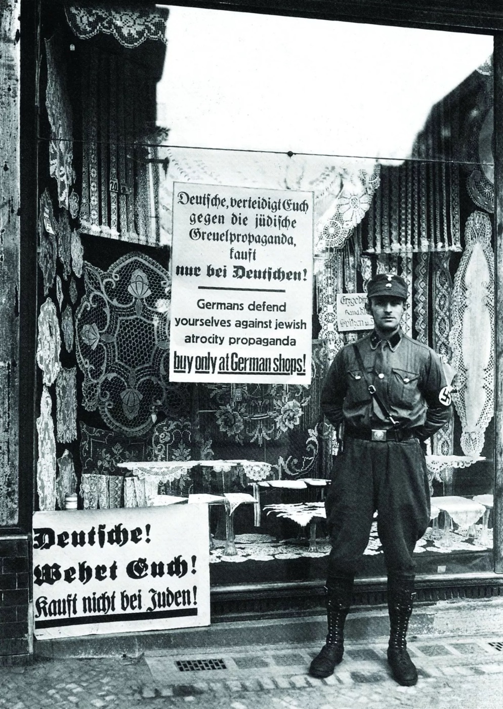 An SA man standing guard beside a shop window that displays a sign reading Kauft nicht bei Juden, during the boycott of April 1933.