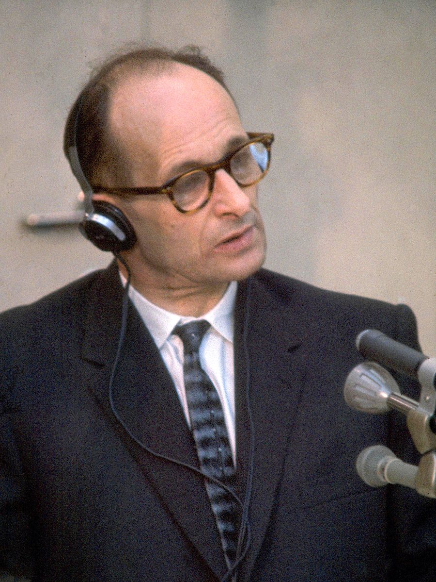A man in glasses and headphones speaking into microphones inside a glass booth at trial