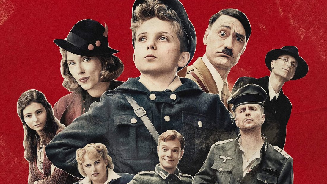 A man dressed as Hitler crouching in a forest talking to a boy in Hitler Youth uniform