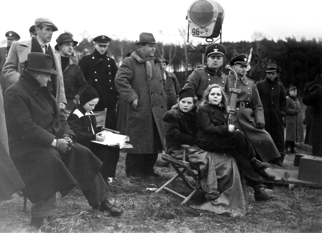 Black and white production photograph of a film crew and costumed cast on a period set