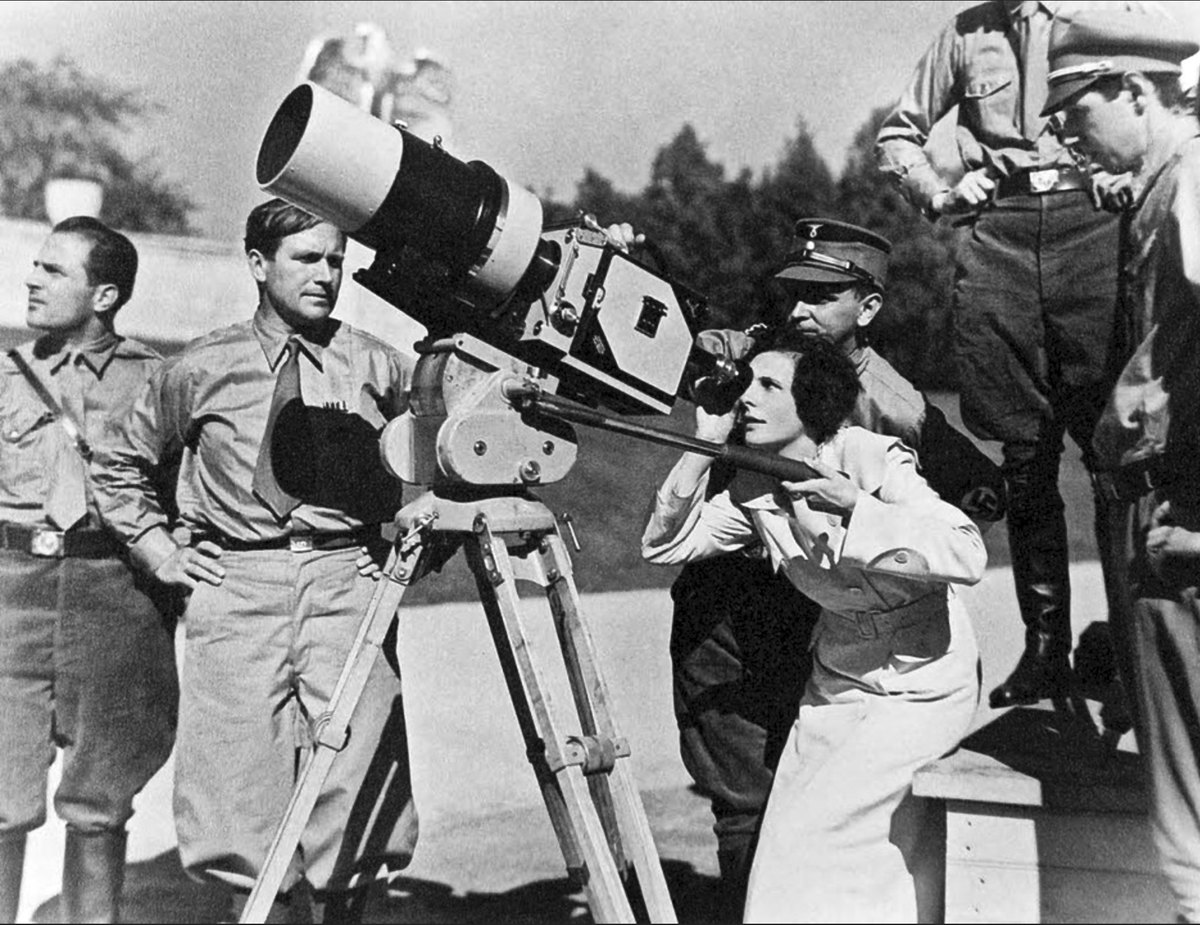 Leni Riefenstahl at a large film camera on a tripod at the Nuremberg rally grounds, surrounded by uniformed SA men