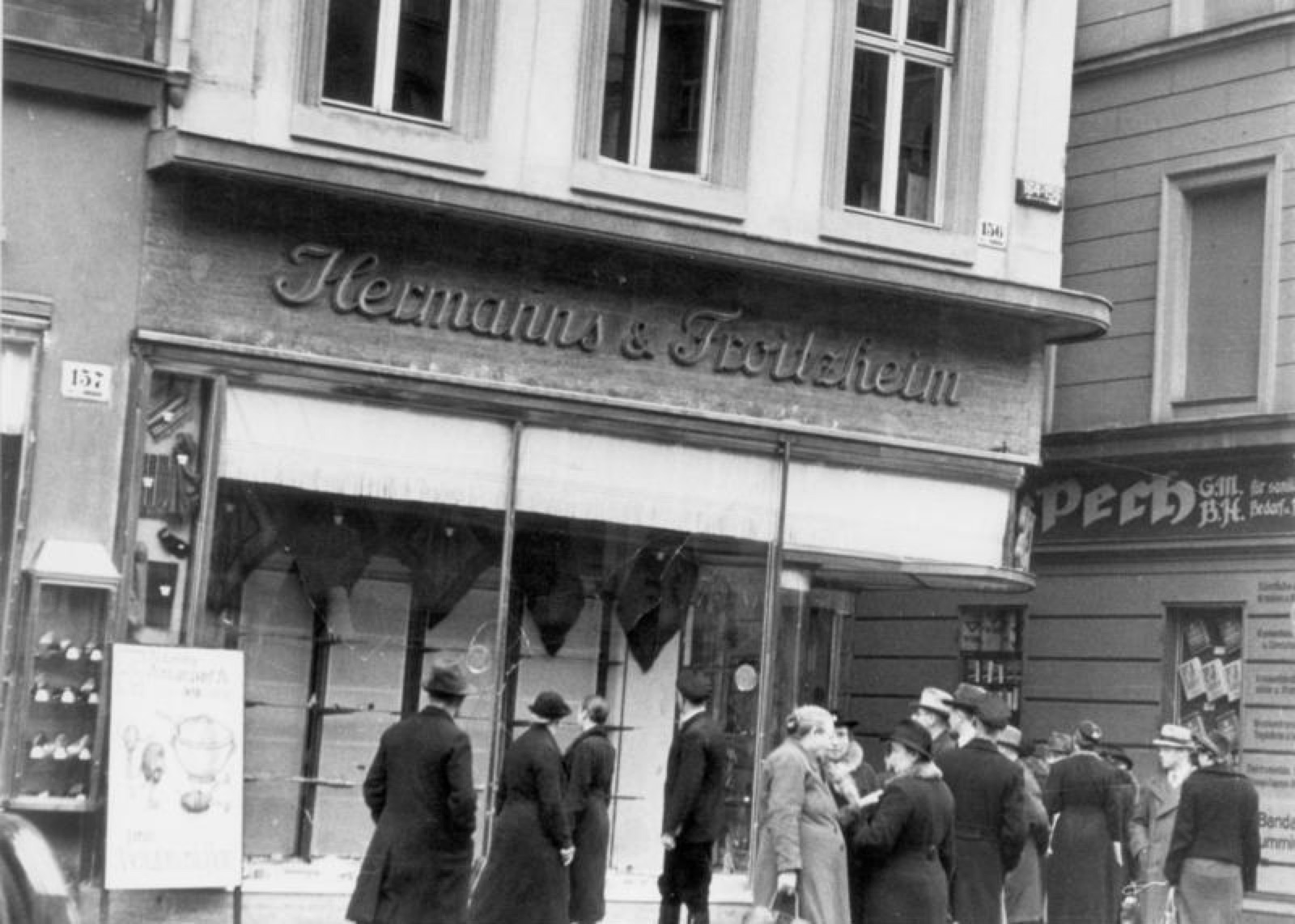 A shop front with its plate glass windows smashed out, shards on the pavement and the display area behind the empty frames disordered.