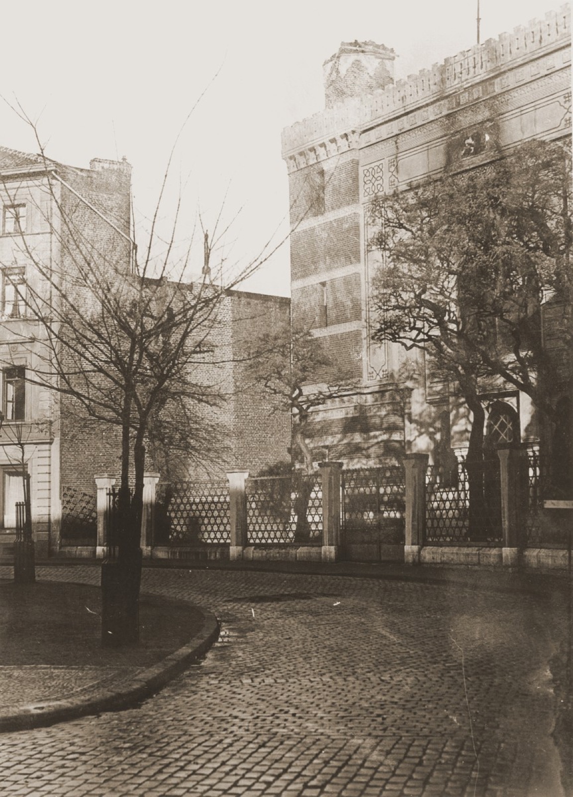 The stone street front of a nineteenth century synagogue, with a tall arched portal and a band of carved Hebrew lettering above the doors.
