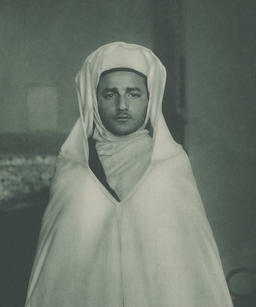 Ceremonial portrait of Sultan Mohammed V of Morocco c. 1927 — white djellaba, red tarboosh, formal court setting.