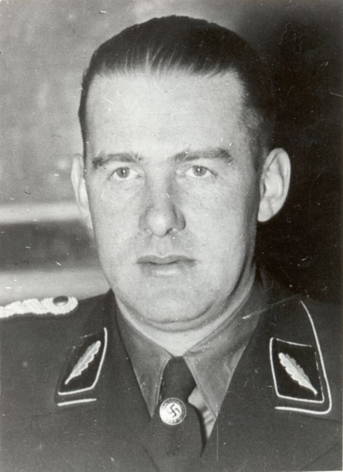 Head-and-shoulders studio portrait of a man in SS uniform and peaked cap, looking slightly off camera.